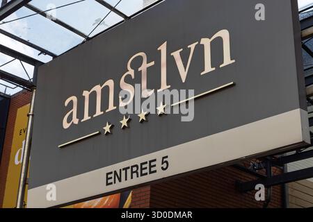 Un cartello esterno per il centro commerciale "amstelveen" (stilizzato come amstlvn), con un logo dorato, quattro stelle e il testo "ENTREE 5" su un retro scuro Foto Stock