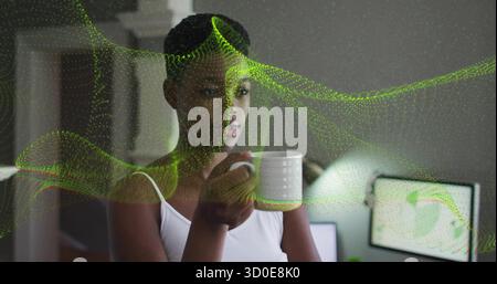 Porta una tazza in ceramica che indossa una canotta nell'ufficio domestico, con i dati di turbolenza verde sui monitor Foto Stock