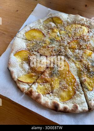 Pizza gourmet condita con sottili fette di pesche fresche, formaggio cremoso gorgonzola e noci sbriciolate su un tavolo di legno. Foto Stock
