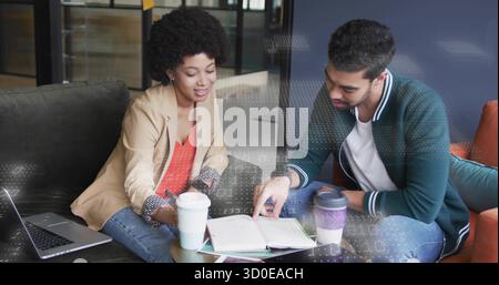 Collaborazione con colleghi che rivedono appunti nella sala d'ufficio, con tazze da caffè per laptop e sovrapposizione tecnologica Foto Stock