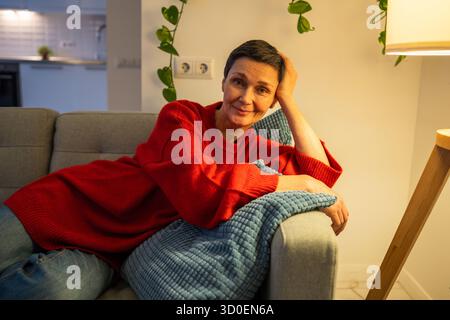Una donna anziana soddisfatta che si appoggia alla testa con il sorriso, guardando la fotocamera con un'atmosfera positiva e contenta Foto Stock