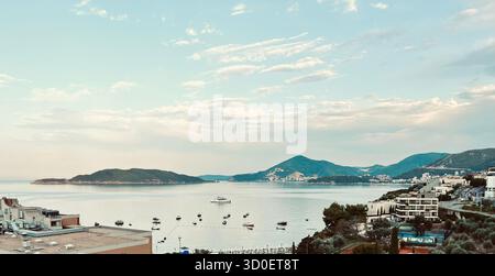 Vista costiera dai toni caldi del mare Adriatico con barche, case sul lungomare e montagne sotto un morbido cielo notturno dorato. Foto Stock