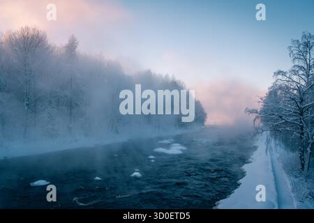 Vapore che si innalza da un fiume in una fredda mattina d'inverno, foresta innevata in Lapponia, Finlandia Foto Stock
