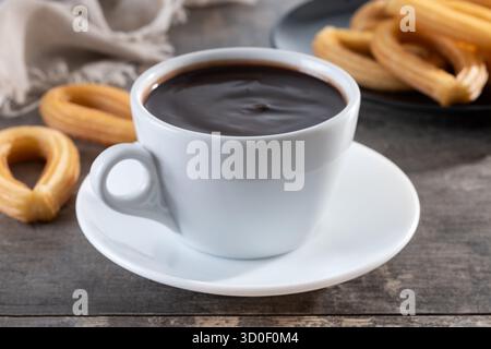 Cioccolata calda spessa in una tazza bianca con churros su un tavolo di legno Foto Stock