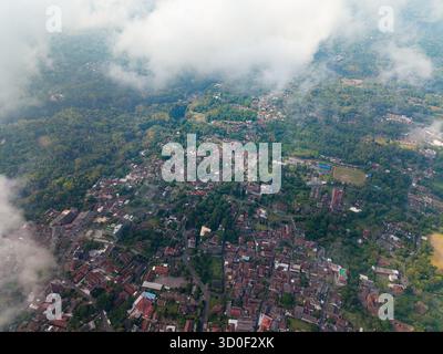 Veduta aerea di una citta' annidata tra lussureggiante vegetazione e avvolta dalla nebbia, Kaliurang, Daerah Istimewa Yogyakarta, Indonesia. Foto Stock