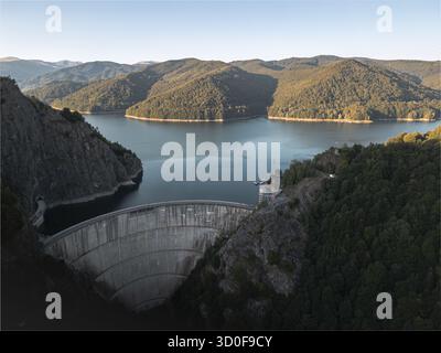 Vista aerea della diga di Vidraru che attraversa il paesaggio con montagne e foreste che circondano il lago blu, Curtea de Arges, Romania. Foto Stock