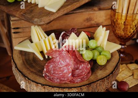 Tagliere rustico di salumi con una selezione di fette di salame stagionato, fuet catalano, spicchi di formaggio semiduro e uva verde fresca Foto Stock