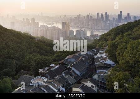 Vista aerea della nebbiosa via Vecchia di Huangjueya annidata tra colline verdeggianti, accostata allo skyline moderno di Chongqing, Cina. Foto Stock