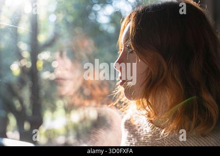 Una giovane donna guarda attentamente fuori dalla finestra Foto Stock