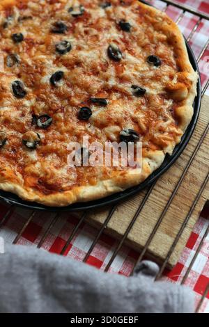 Pizza fatta in casa appena sfornata con olive nere e formaggio fuso su una griglia rinfrescante Foto Stock