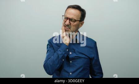 Uomo ispanico che soffre dolori ai denti su sfondo bianco, stringendo la mascella con un'espressione dolorosa, isolato in un contesto maturo senior showi Foto Stock