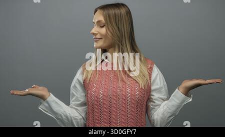Donna sorridente che regge su sfondo grigio isolato indossando gilet rosa e camicia bianca che trasuda felicità e positività Foto Stock