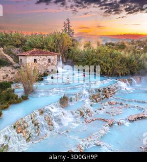 Veduta aerea delle cascate e delle acque azzurre delle sorgenti termali di Saturnia, riscaldate dal sole al tramonto, in contrasto con la pietra aspra, Manciano, Toscana, Italia. Foto Stock