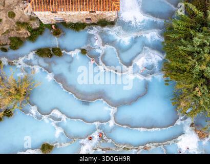 Vista aerea delle acque azzurre che scendono dalle piscine terrazzate di Saturnia, dove le persone si rilassano tra i torrenti che scorrono, Manciano, Toscana, Italia. Foto Stock