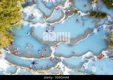 Vista aerea di persone che si rilassano nelle acque azzurre lattiginose delle sorgenti termali che si infrangono sulle terrazze in travertino, Saturnia, Toscana, Italia. Foto Stock