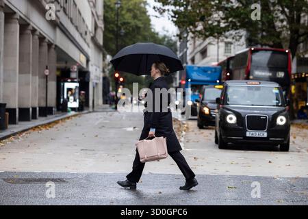 Una donna d'affari londinese attraversa Oxford Street riparandosi sotto un ombrello in un giorno d'autunno bagnato e ventoso, nel centro di Londra, Inghilterra, Regno Unito Foto Stock