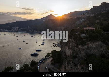 Vista aerea dei raggi dorati del sole che baciano la costa frastagliata dove il mare incontra le scogliere, Taormina, Sicilia, Italia. Foto Stock