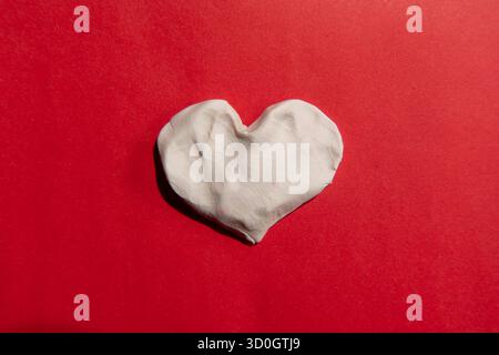 Cuore di argilla bianca su carta rossa Foto Stock