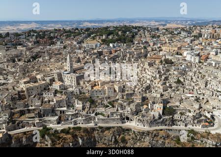 Vista aerea di antiche abitazioni in pietra aggrappate a scogliere rocciose sotto un cielo morbido, un paesaggio senza tempo di architettura baciata dal sole, Matera, Basilicata, Italia. Foto Stock