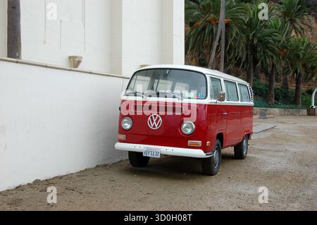 Classico pulmino rosso e bianco Volkswagen parcheggiato accanto a un edificio bianco ad Avalon, l'isola di Catalina, circondato da palme e paesaggi costieri Foto Stock