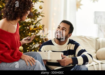 Una coppia gioiosa condivide i momenti speciali accanto all'albero di Natale, scambiandosi regali e sorrisi. Foto Stock