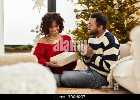 Una felice coppia afroamericana ama il Natale insieme, scambiandosi regali accanto a un albero decorato. Foto Stock
