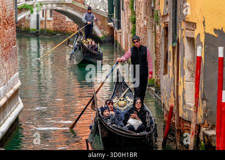 Le persone si godono un giro in gondola mentre un gondoliere guida la gondola lungo uno stretto canale nel sestiere di San Marco a Venezia, Italia Foto Stock