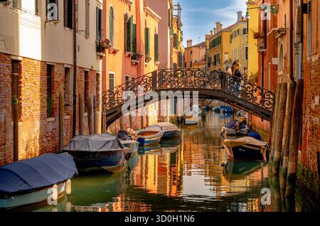 Persone che attraversano un ponte sul canale con colori pastello che si riflettono nel canale Riello de Santa Sofia, nel Cannaregio sestiere di Venezia Foto Stock
