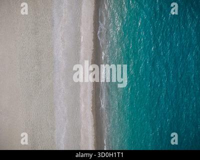 Vista aerea del vivace mare turchese che incontra la spiaggia di sabbia chiara in un incredibile contrasto di bellezza naturale, Marinello, Città metropolitana di Messina, Italia. Foto Stock