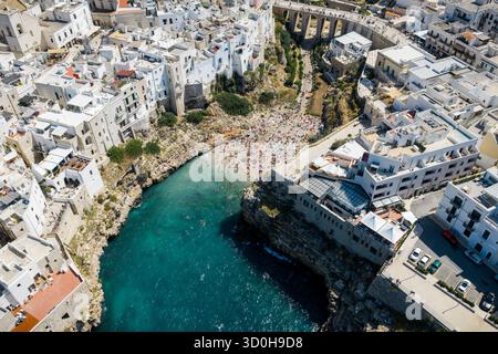 Veduta aerea di una spiaggia vibrante annidata tra edifici bianchi e aspre scogliere, dove le acque turchesi incontrano la sabbia dorata, Polignano a Mare, Puglia, Italia. Foto Stock