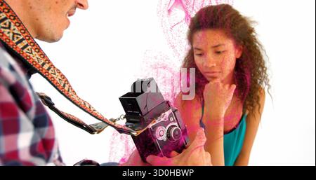 Fotografo in possesso di una fotocamera a doppio obiettivo con cinturino che cattura il modello nella parte superiore in mezzo alla polvere rosa in studio Foto Stock