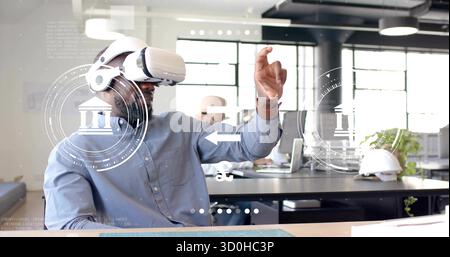 Uomo con gesti che indossa un visore VR bianco che manipola l'interfaccia utente olografica alla scrivania, con casco di sicurezza Foto Stock