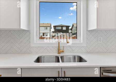 Il lavandino della cucina con rubinetto dorato si trova davanti a una finestra con vista sulle case Foto Stock