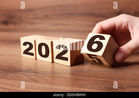 Anno nuovo. Donna che capovolge il cubo con i numeri 5 e 6 per fare 2026 su un tavolo di legno, primo piano Foto Stock