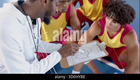 L'allenatore inginocchiato tiene gli appunti e punta gioca sul campo blu, giocatori in maglia gialla accovacciati Foto Stock