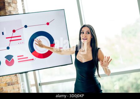 Donna d'affari sicura che offre una presentazione incentrata sull'analisi dei dati e sulla strategia in un moderno ufficio professionale Foto Stock