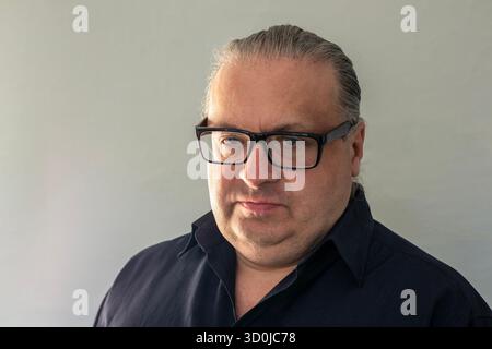 Ritratto professionale di un uomo sicuro di sé con occhiali che indossa una camicia scura su uno sfondo semplice Foto Stock