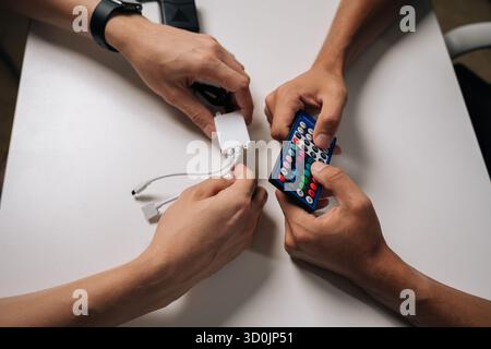 Vista dall'alto ravvicinata di due tecnici che collegano le strisce luminose a LED RGB tramite telecomando e controller, regolando le impostazioni di retroilluminazione per personalizzarle Foto Stock