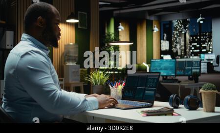 Un analista finanziario maschile esamina i conti di trading e i dati archiviati per i report sui ricavi, utilizzando grafici digitali per pianificare l'allocazione delle risorse e allineare gli obiettivi aziendali al successo finanziario. Foto Stock