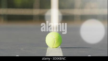 Palla da tennis verde brillante sulla linea bianca sul campo rigido vicino a palo di rete e recinzione a catena Foto Stock