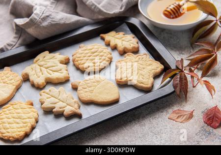 Biscotti appena sfornati a tema autunnale disposti su una teglia da forno con miele e foglie autunnali Foto Stock
