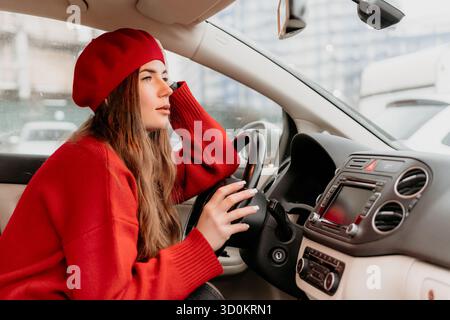 Donna che guida un'auto. Giovane donna in un berretto rosso che guarda con attenzione fuori dal finestrino della sua auto. Foto Stock