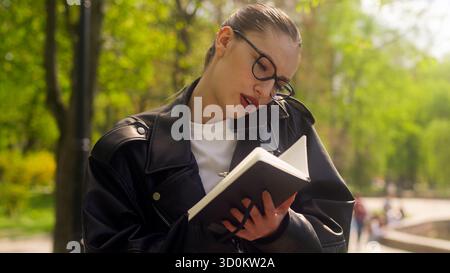Donna d'affari impegnata che parla telefono cellulare smartphone telefono tecnologia di comunicazione lavoro scrittura di chiamate in un parco di progetto notebook lavoro aziendale Foto Stock