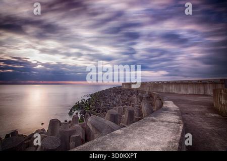 Vista a lunga esposizione della parete marina curva e dei grandi demolitori ondulati di cemento che fanno parte delle difese costiere vicino a Torness Foto Stock