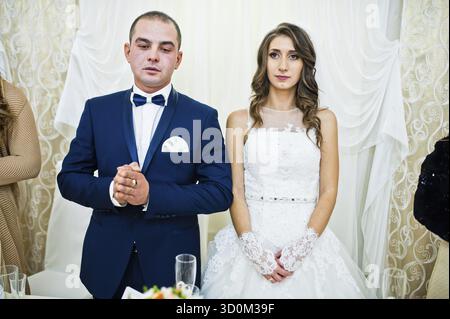 Coppia di nozze al tavolo del ristorante, mani piegate per la preghiera Foto Stock