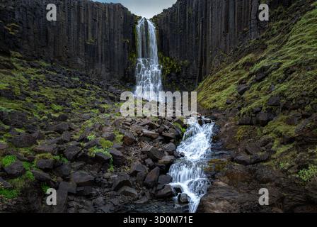 Cascata incorniciata da impressionanti colonne di basalto e scogliere mossy. Foto Stock