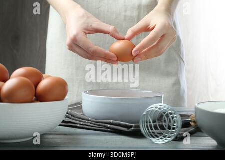 Donna che rompe l'uovo al tavolo all'interno, primo piano Foto Stock