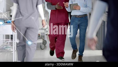 Infermiera che cammina indossando scrub di Borgogna, medico con compressa che condivide le informazioni del paziente nel corridoio dell'ospedale Foto Stock