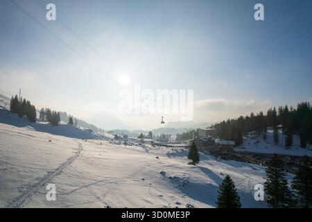 Vista aerea della neve baciata dal sole copre il paesaggio, punteggiato da sempreverdi e impianti di risalita che perforano il cielo, creando un panorama invernale delle meraviglie, Engelberg, Svizzera. Foto Stock