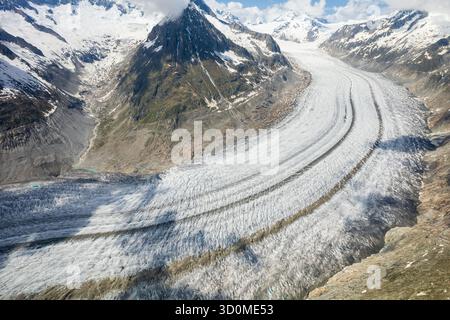 Vista aerea del colossale ghiacciaio Aletsch serpente attraverso le aspre Alpi svizzere spolverate di neve, un fiume ghiacciato che intaglia un sentiero di bianco e grigio contro la terra, la Svizzera. Foto Stock